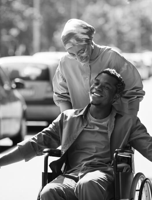 Friends laughing together while one pushes the other who is in a wheel chair