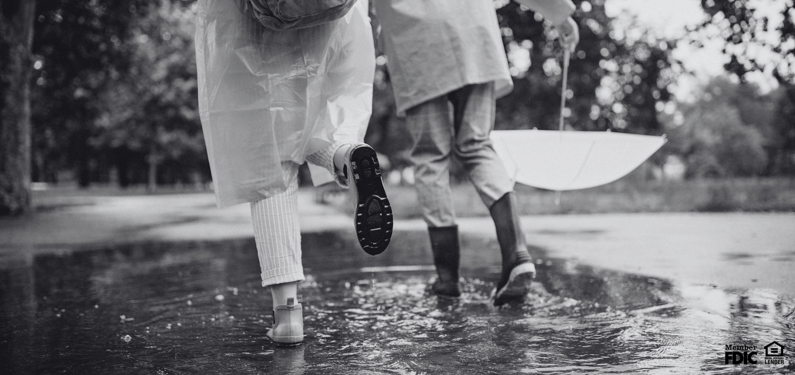 two kids jump in puddles while enjoying the rain outside.